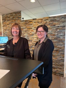 Two staff members posing in front desk